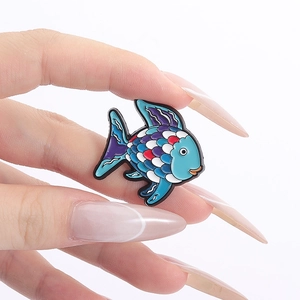 Hand holding a colorful tropical fish enamel brooch with vibrant scales and black outlines