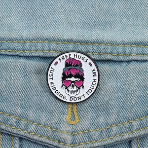 Round pink skull enamel pin with Free Hugs quote on a blue denim jacket pocket