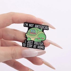 Detail showing an enamel turtle brooch with a house shell and stay at home quote