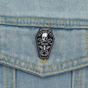 Coffin shaped Memento Mori enamel pin on denim jacket featuring skull and hourglass