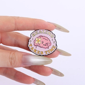 Gros plan d'un badge en émail rose cerveau avec texte de guérison entre les doigts