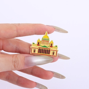 Detail of St. Isaac's Cathedral enamel brooch pin held between fingers on white background
