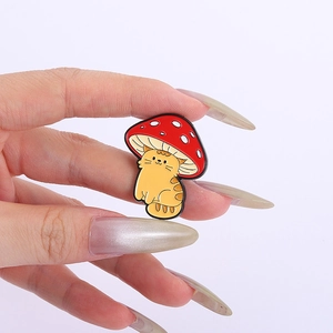 Gros plan d'un pin's en émail avec un chat orange sous un champignon rouge