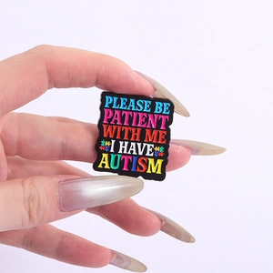 Macro shot of a black enamel pin with colorful autism awareness text and puzzle pieces
