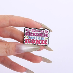 Close-up of enamel pin with My illness is CHRONIC but I am ICONIC slogan and pink details