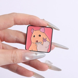 Close-up showing the size of a square enamel pin with a cute orange rock-and-roll hamster