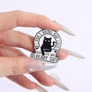 Close-up of funny black cat enamel pin held by hand featuring humorous English text
