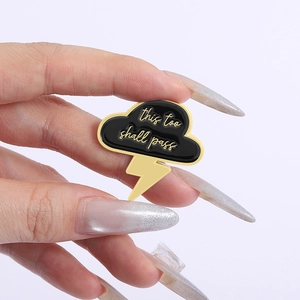 Macro shot of black enamel cloud brooch with gold thunder and this too shall pass text