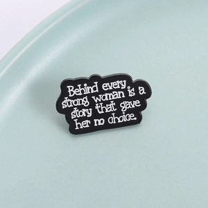 Broche en émail noir avec texte blanc: Behind every strong woman is a story en détail