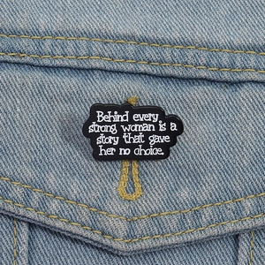 Broche en émail noir avec texte inspirant sur une veste en jean bleu clair