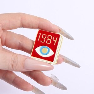 Macro shot of a red 1984 book enamel pin with a blue eye symbol held in hand