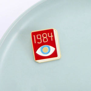 Creative red 1984 book enamel pin with blue eye motif on a ceramic display