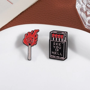 Gothic skull matchbox and flaming match enamel pins set displayed on a ceramic dish