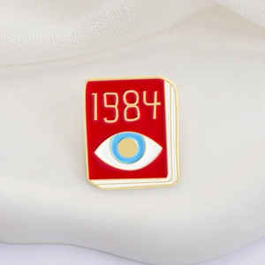 Red 1984 book enamel pin featuring a blue eye design and elegant gold-plated metal edges
