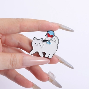 Macro detail of a white cat enamel pin holding a wine glass shown on a person's hand