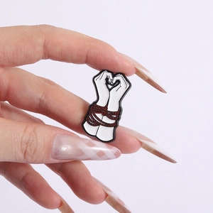 Detail of unique hand heart enamel pin showing red rope binding and creative gesture