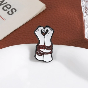 Creative enamel pin with hands tied by red rope forming a heart shape on white plate
