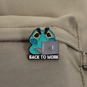 Detail of green frog enamel pin with BACK TO WORK text on khaki nylon backpack