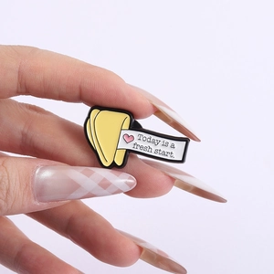Macro shot of fortune cookie enamel pin with Today is a fresh start quote on hand