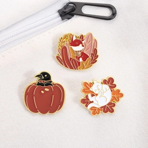 Detail view of fox, cat and crow enamel pins with fall pumpkin theme on canvas