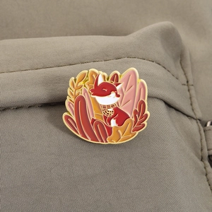 Detail of fox enamel pin with scarf and autumn leaves on canvas backpack texture