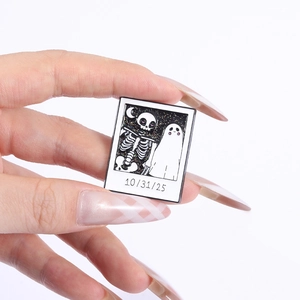 Gros plan d'un pin's d'Halloween style Polaroid avec squelette et fantôme tenu en main