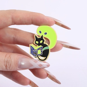 Détail d'un pin's émaillé montrant un fantôme lumineux et un chat noir lisant un livre