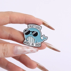 Detail of blue whale enamel pin featuring Everything Whale Be Okay pun and sunglasses