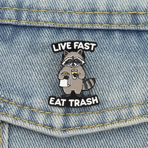 Funny raccoon enamel pin with Live Fast Eat Trash slogan on denim jacket