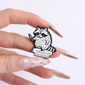 Detail of creative raccoon enamel pin badge with i require snacks text on white background