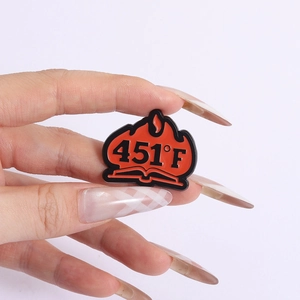 Close-up of 451°F burning book enamel pin with vibrant red flames and black metal details