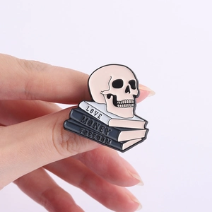 Detail of skull enamel pin with Love, Money, and Freedom text on stacked books