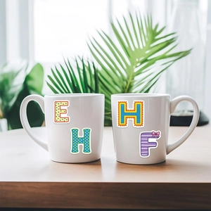 Pair of white ceramic mugs with colorful cartoon alphabet letters on a wooden table
