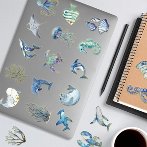 Close-up of gold-stamped ocean creature stickers on a laptop and notebook surface