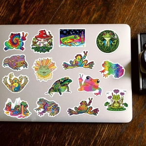 Detail of psychedelic frog stickers on silver laptop surface against dark wood