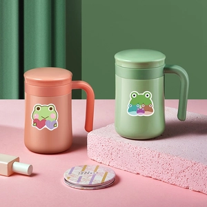 Cute green and coral mugs with frog stickers and lids on a colorful geometric background