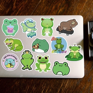 Flat lay of cartoon frog stickers on silver laptop over a dark wood background