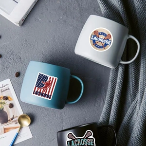Three lacrosse themed ceramic mugs in black, blue and white on a cozy grey knit blanket