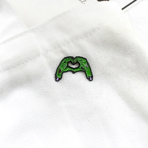 Detail of green zombie hand heart enamel pin on a white canvas background texture