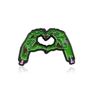 Green zombie hands forming heart gesture enamel pin with stitching and bone details