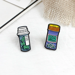 Dettaglio di spille in smalto con flaconi di medicinali Chill Pills e Love Me