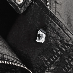 Enamel pin of long-haired woman with witch hat taking a selfie on black leather background