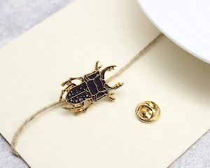 Detailed close-up of golden beetle brooch with black enamel inlay on beige card paper