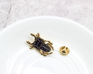 Detailed close-up of a beetle-shaped brooch in black enamel and gold finish with butterfly clutch