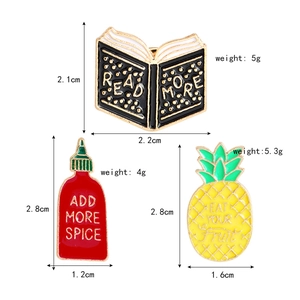 Macro shot of cartoon enamel pins showing Read More book, spice bottle, and pineapple details