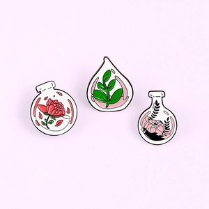 Detailed view of three enamel flower bottle pins featuring floral designs on purple background