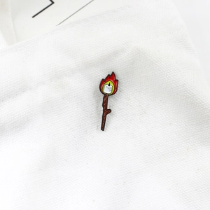 Creative enamel brooch featuring a marshmallow roasting over fire on a wooden stick