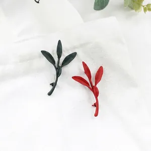 Matte leaf-shaped alloy brooches in red and dark green on a white canvas bag