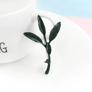 Detailed macro shot of dark green leaf brooch pinned on a white ceramic mug rim
