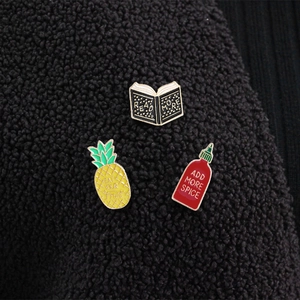 Cute enamel pin set with pineapple, open book, and red sauce bottle on fleece background